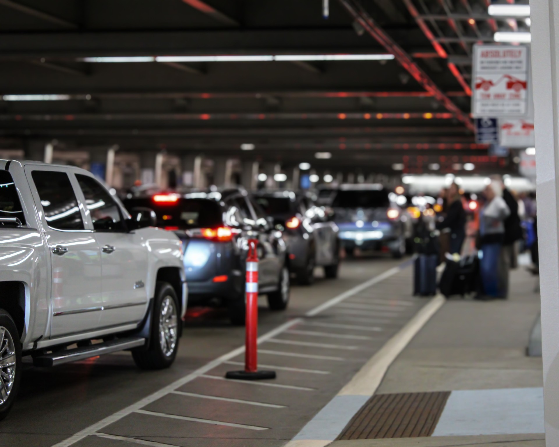 An airport terminal arrival pick-up area outside with a line of vehicles and blurred people with luggage