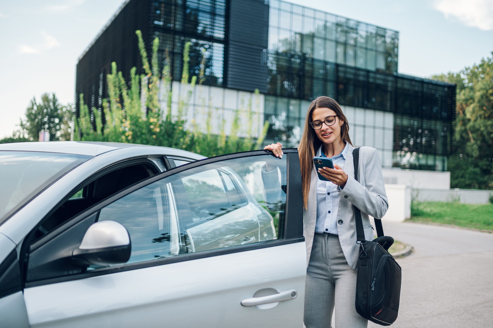 Business woman getting into the car and using smartphone